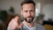 © Bussakon - A man with a beard points directly at the viewer with a confident and engaging expression in a softly blurred indoor setting