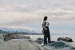 © SHOTPRIME STUDIO - Woman in casual clothes stands on rocky shore looking at cloudy sky over calm sea. Concept of solitude, contemplation, and nature connection during overcast weather outdoors.