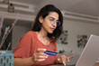 © fizkes - Woman pay household bills or taxes using card and e-bank on laptop, sit at table in living room, send money, check recent credit card transactions, looks at screen with serious or concerned expression