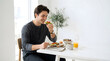 © Lyrick - Smiling man eating healthy balanced breakfast with avocado toast, egg, granola and coffee at home
