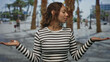 © Krakenimages.com - Young woman holding palms up in a shrug pose on a city street wearing a black and white striped shirt; thoughtful balance.