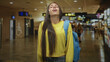 © Krakenimages.com - Woman student with blue backpack and yellow sweater smiling with head tilted back showing braces in airport concourse; relief travel anticipation.