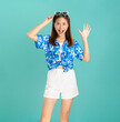 © sitthiphong - Young Asian woman wearing floral shirt exudes happiness, displaying a joyful expression as she stands against a blue background.