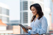 © Home-stock - Happy European entrepreneur lady using digital tablet on city street, working online in urban area outside, free space. Technology and career success