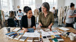 © Ace - Diverse creative team of professional female fashion designers collaborating and examining various colorful fabric swatches and clothing patterns scattered across a large wooden studio workspace desk
