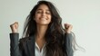 © CLARET - Young woman celebrating success with closed eyes and clenched fists, wearing a business suit.
