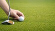 © ภัทรดนัย บุญชูเดชะ - hand placing golf ball on green with putter, close up golf setup on putting green, preparing to putt on smooth turf, golfer aligning ball and club, sports equipment on grass.