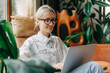 © Ilona - Happy smiling blonde woman using a laptop to work remotely.