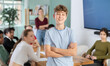 © JackF - Confident teenage boy standing with his back to classmates sitting at table in classroom