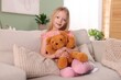 © New Africa - Little girl hugging her teddy bear on sofa at home