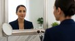 © Lucianastudio - Confident professional woman applying makeup in mirror before work preparing for success in business career