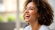 © Hasaranga - A smiling woman with curly hair laughing joyfully indoors.