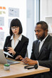 © sofiko14 - A woman in glasses points at a document while a man listens intently during a business meeting, discussing strategy