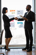 © sofiko14 - A professional handshake between a businesswoman and an African American businessman in an office setting with charts on the wall