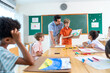 © narong - Wide shot of the teacher stand beside and try to make a boy with blond hair present his drawing or painting in front of the classroom and also ask the idea or the meaning of the picture.