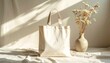 © Lela - Aesthetic light beige tote bag with dried flowers in a vase and soft shadows on a textured surface