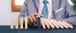 © Smile Studio AP - Businessman hand stopping falling domino blocks to prevent chain reaction, symbolizing risk control, leadership, and strategic decision making