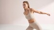 © Tina - A young woman with long blonde hair performs a stretching exercise in a light-colored athletic outfit against a soft pink background.