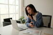 © Parichat - Young woman talking on phone while working with laptop and analyzing data