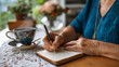© Maksym - Elderly woman writing resolutions in leather journal at kitchen table, morning tea steam rising, handwritten goals visible on aged paper, warm natural light through lace curtains,