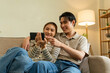 © MIND AND I - Happy Young Asian Couple Watching Smartphone Together on Sofa at Home