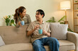 © MIND AND I - Happy Young Asian Couple Smiling and Drinking Coffee Together at Home