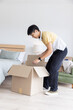 © wavebreak3 - Large open cardboard moving box sitting on light wood floor near low bed and green sofa