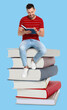 © New Africa - Man sitting on stack of big books and reading book against light blue background
