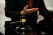 © NanSan - Close-up of judge gavel on desk with blurred lawyer gesturing in background, courtroom or legal office setting, shallow depth of field.
