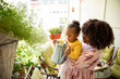 © Marko Geber - Mother and toddler watering plants on apartment balcony