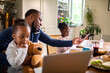 © Marko Geber - Father multitasking with daughters during remote work at kitchen table