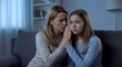 © ArtMajestic - Woman whispering secret to daughter sitting on couch. Mother sharing confidential Information with kid. Family communication, worry and emotional support concept in home evening interior