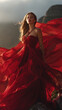 © valeo5 - Stunning Young Woman in a Flowing Red Silk Gown Posing Against a Dramatic Mountain Backdrop During Golden Hour; Elegant Fashion Photography Featuring Ethereal Chiffon Fabric Waving in the Wind