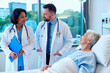 © DragonImages - Senior Caucasian woman resting in hospital bed while multiethnic doctors consulting during bedside visit, representing patient care and teamwork. For healthcare marketing and clinic communication