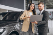© anatoliycherkas - Salesperson showing car options and prices to female client on laptop, making a car purchase decision