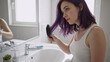 © Vyatcheslav - Young woman with purple hair brushing it in a bright bathroom. Female morning beauty routine and personal care at home