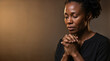 © Faith Stock Studio - Black woman praying with eyes closed and clasped hands. Religious faith and spirituality concept. Studio portrait with copy space on dark background