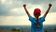 © Viktor - Child wearing red cap raises arms in victory pose. Girl stands outdoors in scenic landscape with cloudy sky. Feeling of success, confidence and accomplishment.