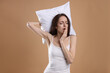 © New Africa - Woman with pillow yawning on beige background