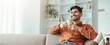© Prostock-studio - A man is sitting on a couch in a well-lit living room. He holds a cup of coffee and smiles as he looks relaxed. Light comes through the window, creating a warm atmosphere in the space.