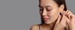 © Pixel-Shot - Young Asian woman putting on beautiful earrings against grey background with space for text