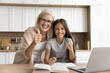 © fizkes - Portrait of girl and her older granny show thumb up. Cute little child studying online using laptop with help of grandmother in kitchen, smile, looking at camera. Effective learning, results, tuition