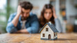 © Nova Zigres - Financial Stress and Mortgage Concept: Young Couple in Despair Behind Small House Model