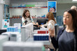 © DC Studio - African American client uses a phone for NFC payment at the checkout counter, purchasing prescription medicine, healthcare items and pharmacy products in a clean organized dispensary.