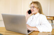 © muse studio - Young woman engaged in a lively phone conversation while working on her laptop in a bright, modern office space