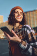© SHOTPRIME STUDIO - woman smile phone urban beanie plaid candid golden - A candid lifestyle portrait of a smiling woman holding a phone in city light, authenticity and golden hour glow, mindful living and emotional