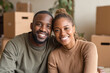 © Kowit - A happy couple smiles together in their new home surrounded by moving boxes and indoor plants.