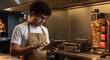 © Myimages - Arab man chef managing online orders on tablet in fast food restaurant kitchen with shawarma cooking