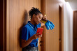 © Drazen - Exhausted black commercial cleaner using cell phone during her break at work.