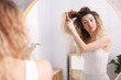 © New Africa - Unhappy woman trying to brush her tangled hair near mirror in bathroom